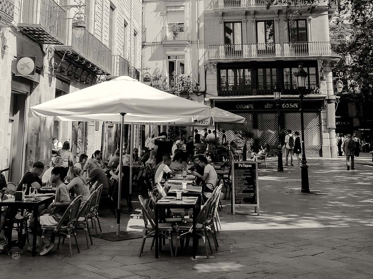 A busy café terrace in the Gothic Quarter, parasol open and people talking over lunch